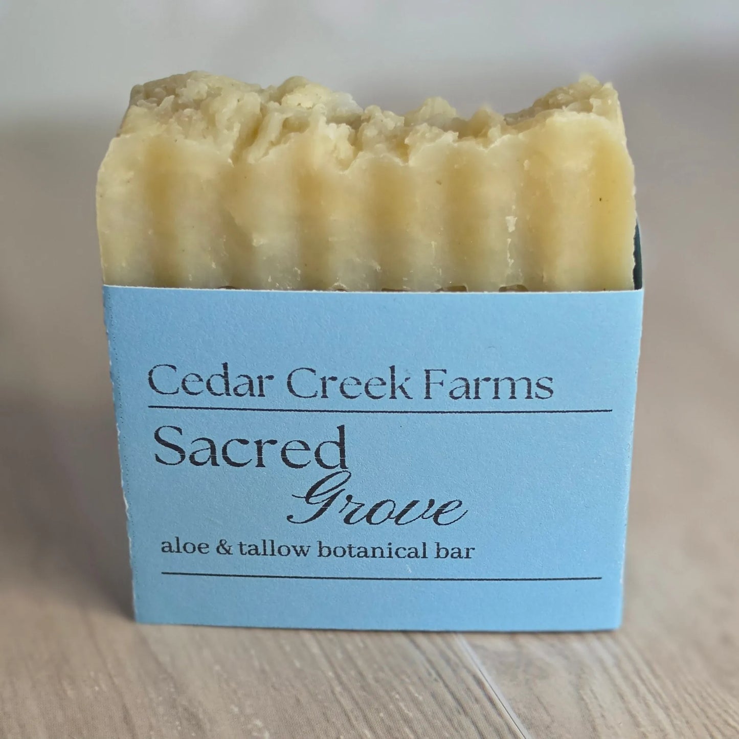 Cedar Creek Farms Sacred Grove Botanical Bar front label close-up showing aloe and tallow botanical soap bar with blue label on wooden surface
