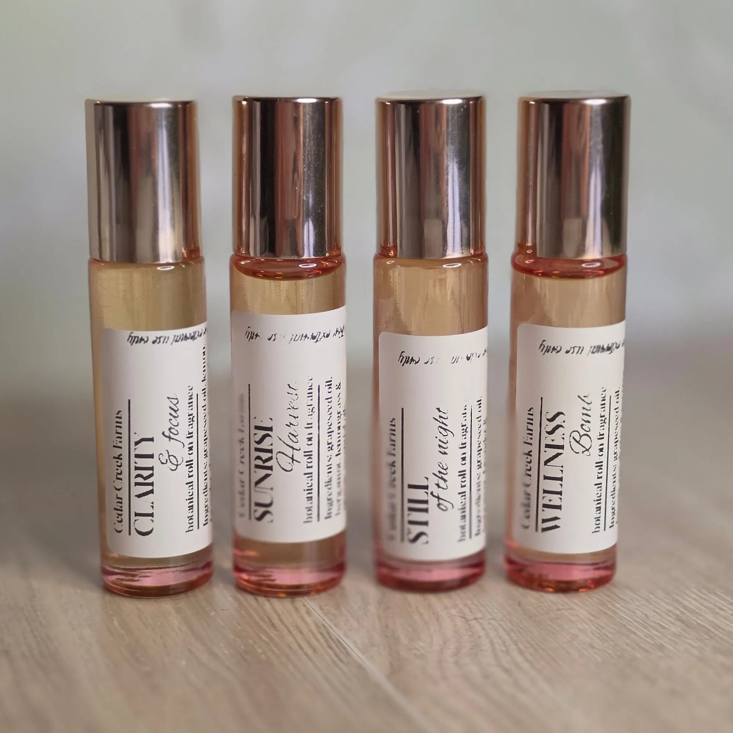 Cedar Creek Farms Botanical Roll-On Fragrance Collection front group display view showing multiple roller bottles including Clarity & Focus, Sunrise Harvest, Still of the Night, and Wellness Bomb on wooden surface
