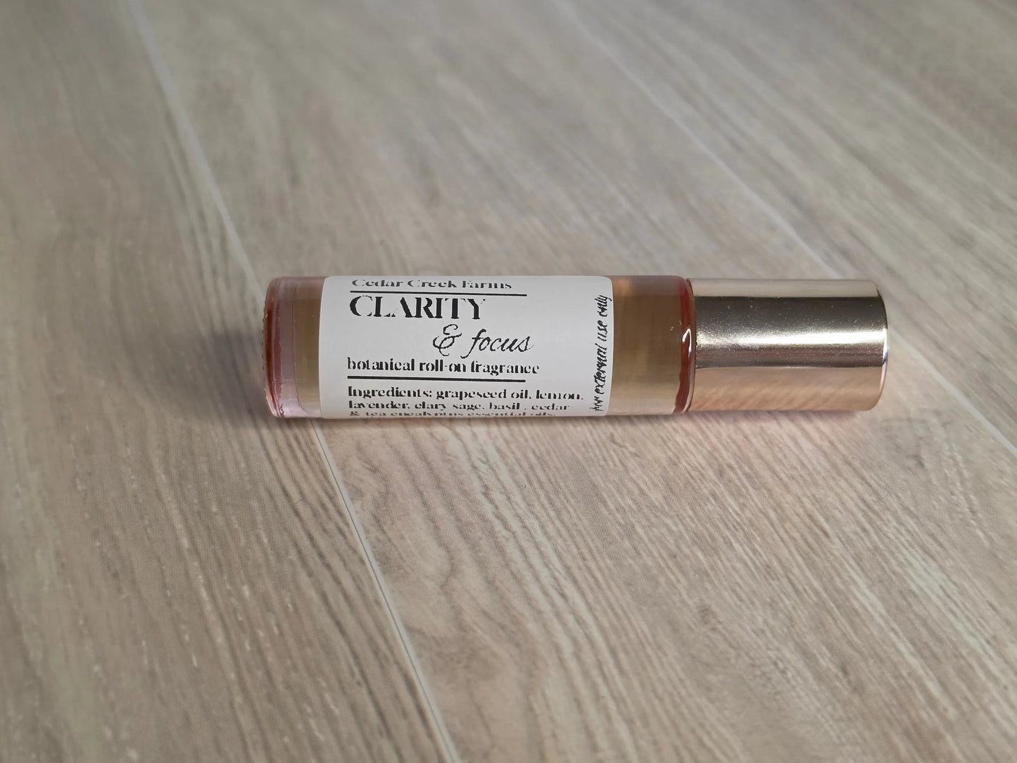 Cedar Creek Farms Clarity & Focus Botanical Roll-On product side profile view showing glass roller bottle with label on wooden surface