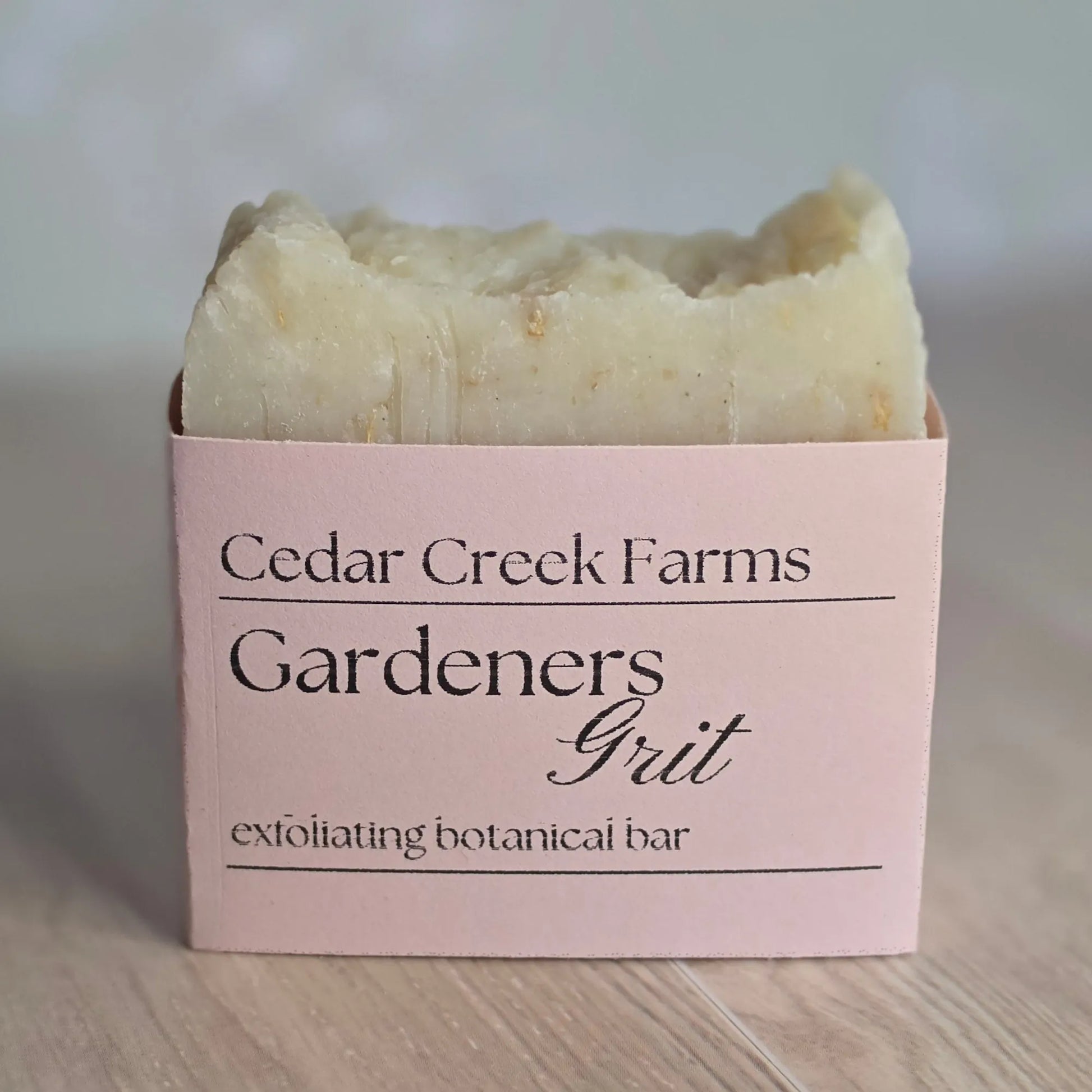 Cedar Creek Farms Gardeners Grit Botanical Bar front label close-up showing exfoliating soap bar with pink label on wooden surface