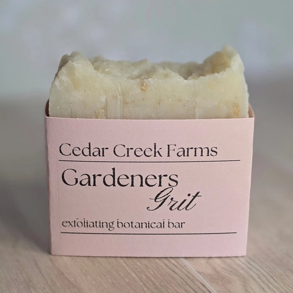 Cedar Creek Farms Gardeners Grit Botanical Bar front label close-up showing exfoliating soap bar with pink label on wooden surface