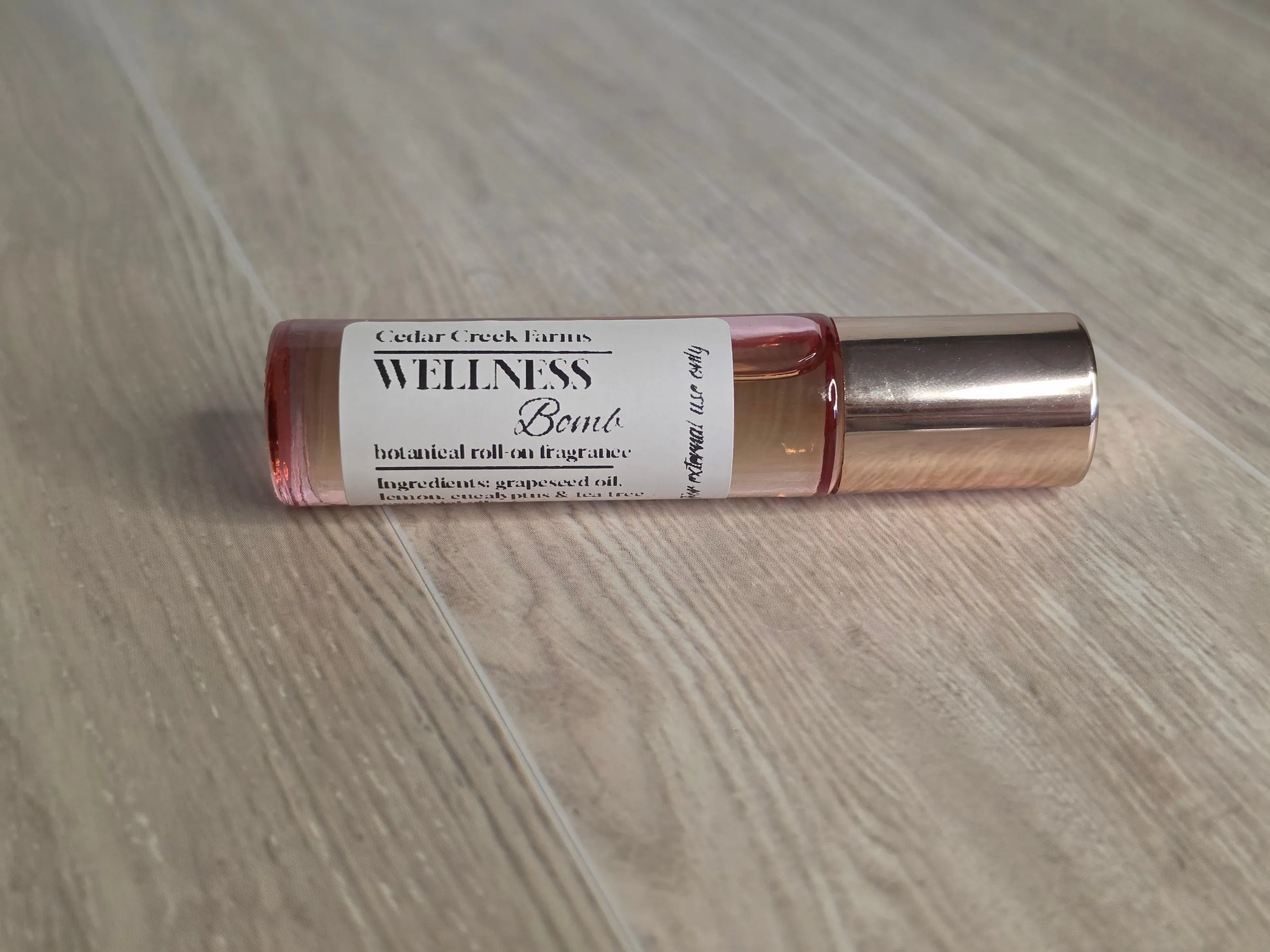 Cedar Creek Farms Wellness Bomb Botanical Roll-On Fragrance side view showing glass roller bottle with metallic cap on wooden surface
